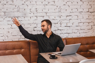 Business man with the laptop has raised a hand in cafe, calling