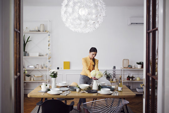 Woman Arranging Flowers At Dinning Table In Home