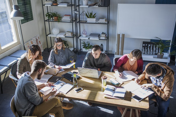 High angle view of students studying at table by window in classroom