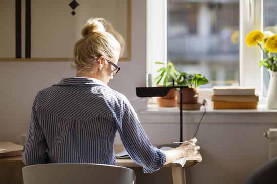 Rear view of woman writing while sitting at table