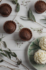 Obraz na płótnie Canvas food photo, chocolate muffins and cupcakes white cream in ceramic plates of handwork on a white wooden background with green eucalyptus and baby's breath top view