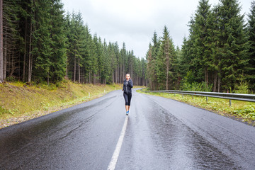 Young athletic woman jogging on rainy hillside road