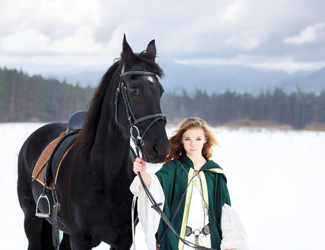 Young girl in white dress with black thoroughbred horse on winter field. Historical equine background