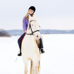Fototapeta premium Young girl in helmet riding white horse on winter field