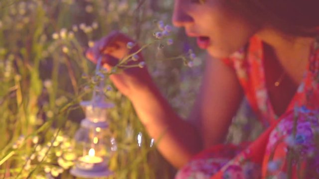 Beautiful girl with lantern finding magic lights in grass at night. Surprised young woman in twilight. Slow motion video footage240 fps, full HD 1080p