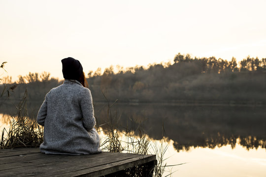mist over the lake. reeds and the girl sitting on a wooden jetty
