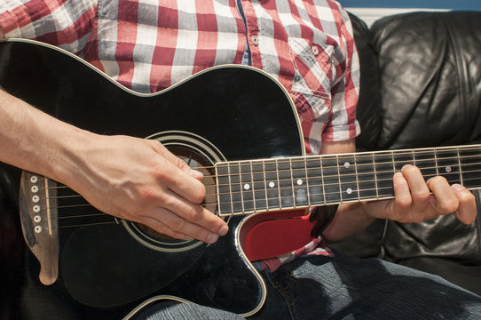 Playing chords on a black acoustic guitar
