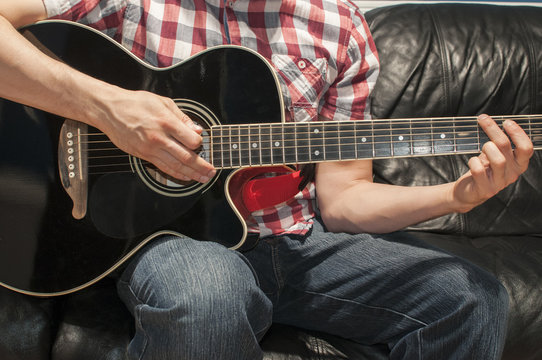 Man playing music on an acoustic guitar on a couch

