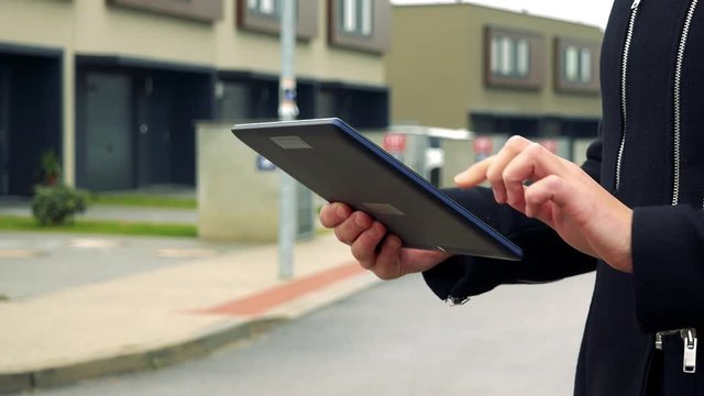 A woman stands on the street in a suburban area and works on a tablet - a street in the background