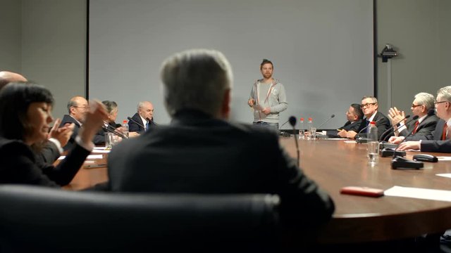 Large audience admires a report and begin clapping. Two young speakers make successful presentation of their new start-up product.
