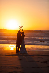 The bride and groom hold drone at sunset near ocean