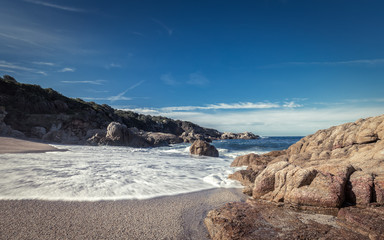 Fototapeta na wymiar Waves wash onto a small sandy cove near Calvi in Corsica