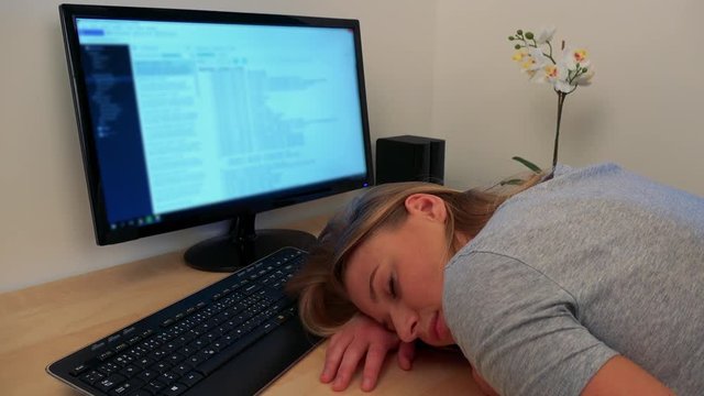 A young, beautiful woman sleeps on a desk in front of a computer