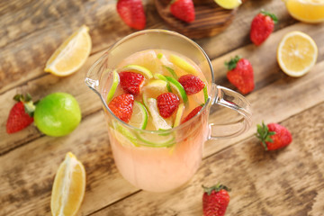 Jug with fresh berry and citrus cocktail on wooden background
