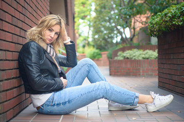 Young attractive serious woman sitting near brick wall