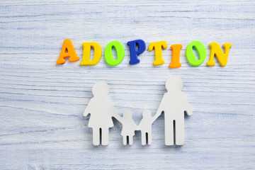 Word ADOPTION and figure in shape of family on light wooden background