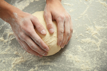 Male hands kneading dough on sprinkled with flour table, closeup