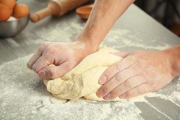 Male hands kneading dough on sprinkled with flour table, closeup
