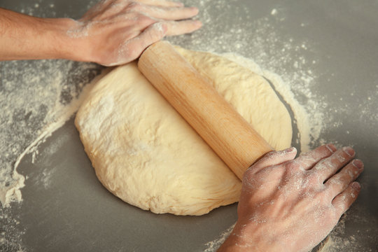 Man rolling out dough on kitchen table, close up