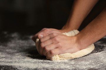 Male hands kneading dough on sprinkled with flour table, closeup