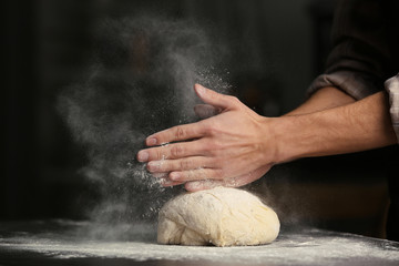 Male hands clapping and sprinkling flour over dough on black background