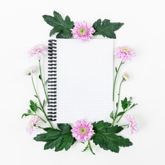 Floral pattern with pink flowers, green leaves and notebook on white background. Flat lay, top view. Woman workspace. Valentine's background