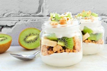 Kiwi, banana, coconut parfaits in mason jars, still life against a white brick background