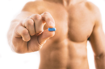 Muscular young man holding blue pill isolated on white background