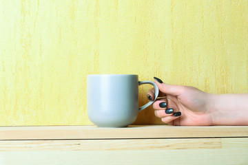 blue tea or coffee cup in hand on yellow background