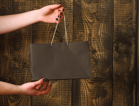 black shopping bag in female hands on wooden background