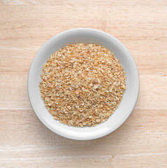 Top view of dried minced garlic in a small bowl atop a wood table. 