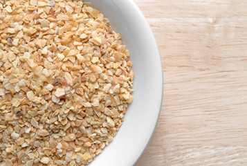 Top close view of dried minced garlic in a small white bowl atop a wood table. 
