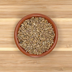Organic milk thistle seeds in a small bowl top view on a wood cutting board.