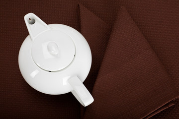 top view of a white teapot and tea strainer on a brown  tablecloth