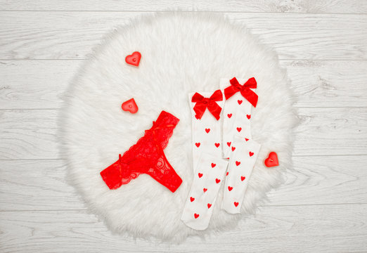 Fashion concept. Red thong panties and white stockings with bows, candles in the shape of a heart on a white fur. View from above