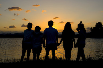 silhouette group of friends standing hand in hand in sunset.