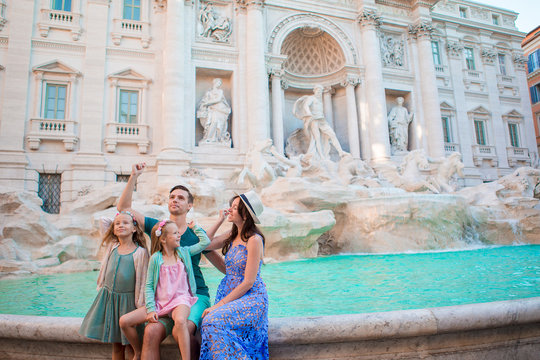 Happy Family Trowing Coins At Trevi Fountain, Rome, For Good Luck. Little Girls And Parents Making A Wish To Come Back.