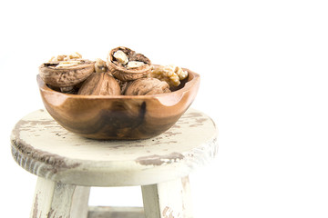 Walnuts in a wooden bowl on a stool with a high key white background