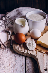 Ingredients for baking Easter cake - eggs, flour, milk, butter, sugar) and utensils on white wooden background. Baking dark background with copy space