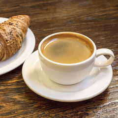 Cup of dark coffee with cereal croissant