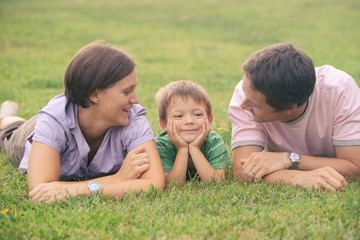 happy blond caucasian kid outdoor family portrait at park with his mum  and dad