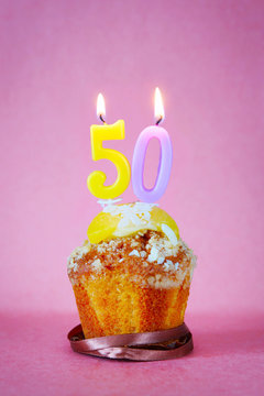 Muffin with burning birthday candles as number fifty on pink background