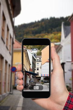 Hand with a smartphone on a background of city streets in Europe. Traveller photographed building, background.