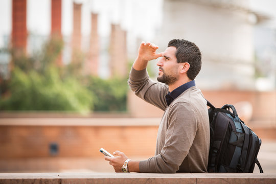 young man with smartphone look away covering eyes with hand urban city