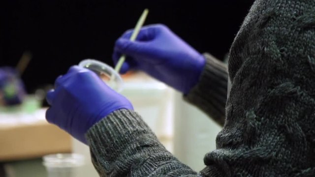 Hands in gloves of a professional painter stir the paint brush. Design studio. Slow motion.