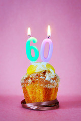 Muffin with burning birthday candles as number sixty on pink background