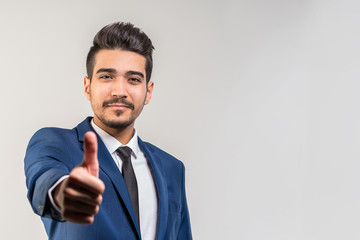 Young attractive man in a blue suit showing thumb up on a gray background. Isolated