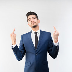 Young attractive man in a blue suit showing middle fingers on a gray background. Isolated