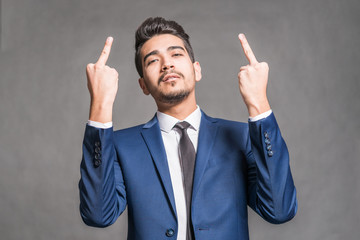 Young attractive man in a blue suit showing middle fingers on a gray background