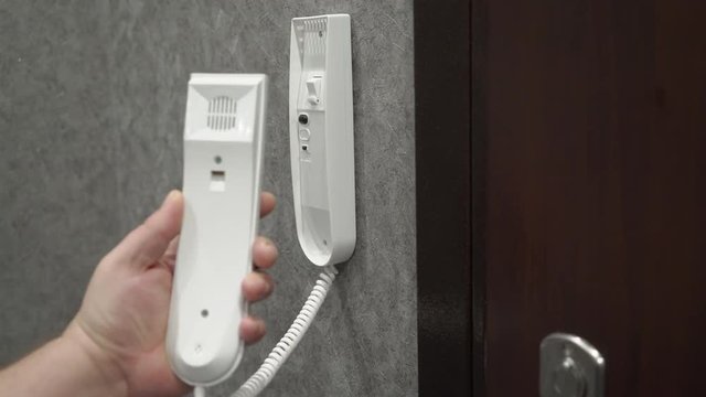 Person holding handset of intercom system installed on a wall in the apartment answering a call